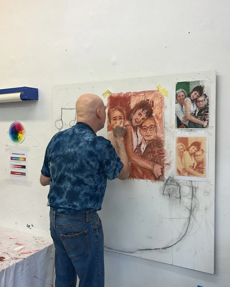 Alumno dibujando un retrato familiar a partir de fotos, en la pared del taller