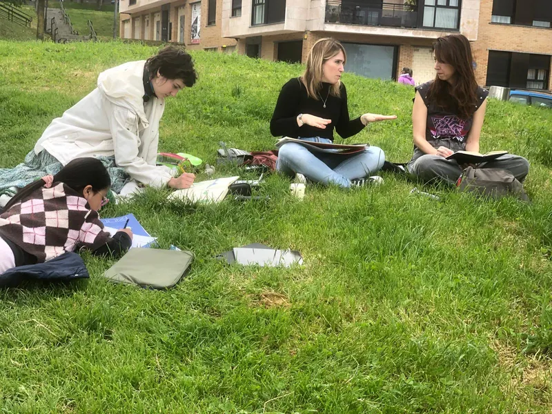 Grupo de alumnas dibujando y charlando sentadas en la hierba, al aire libre