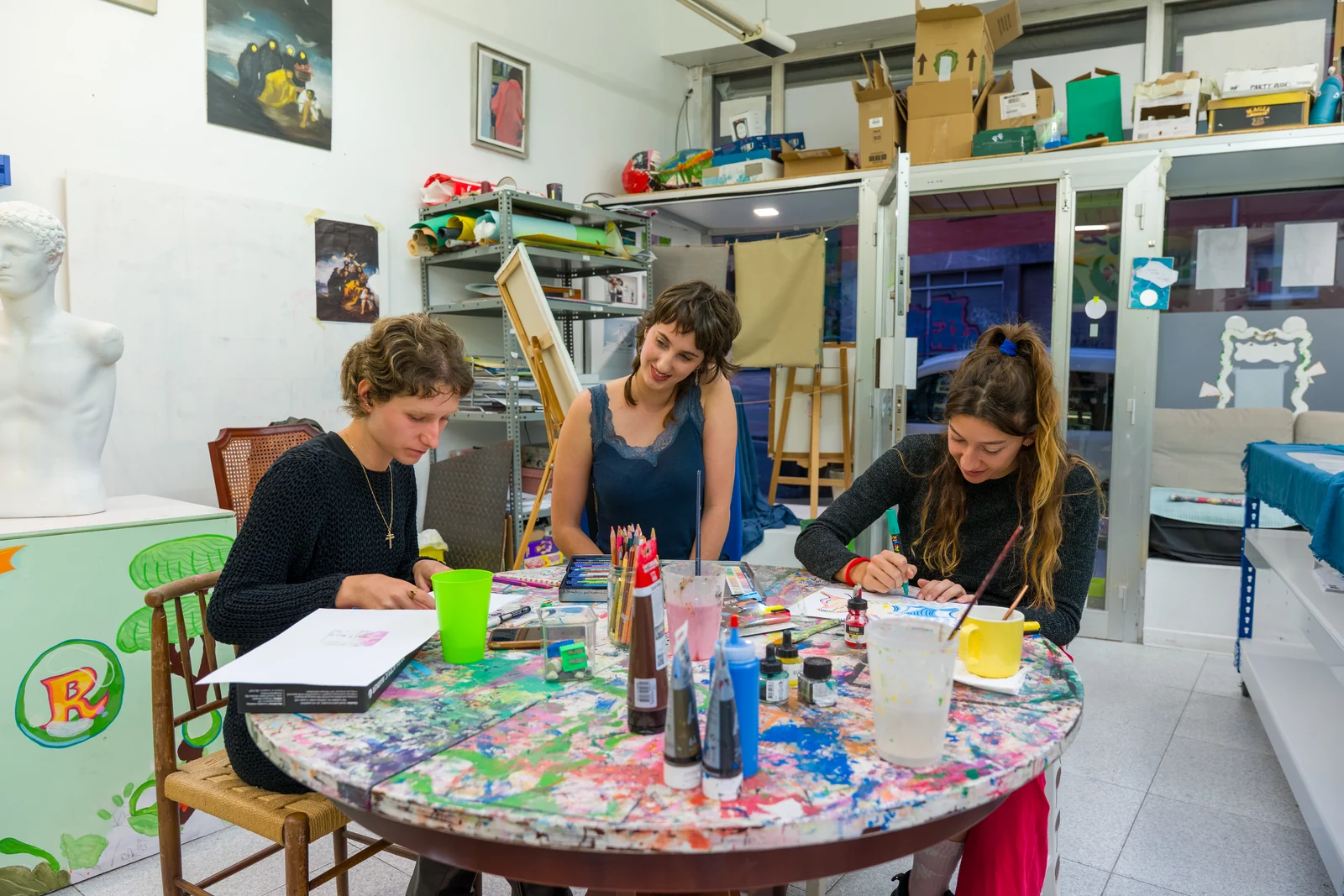 Tres personas pintando juntas en una mesa redonda del taller BiGGeR