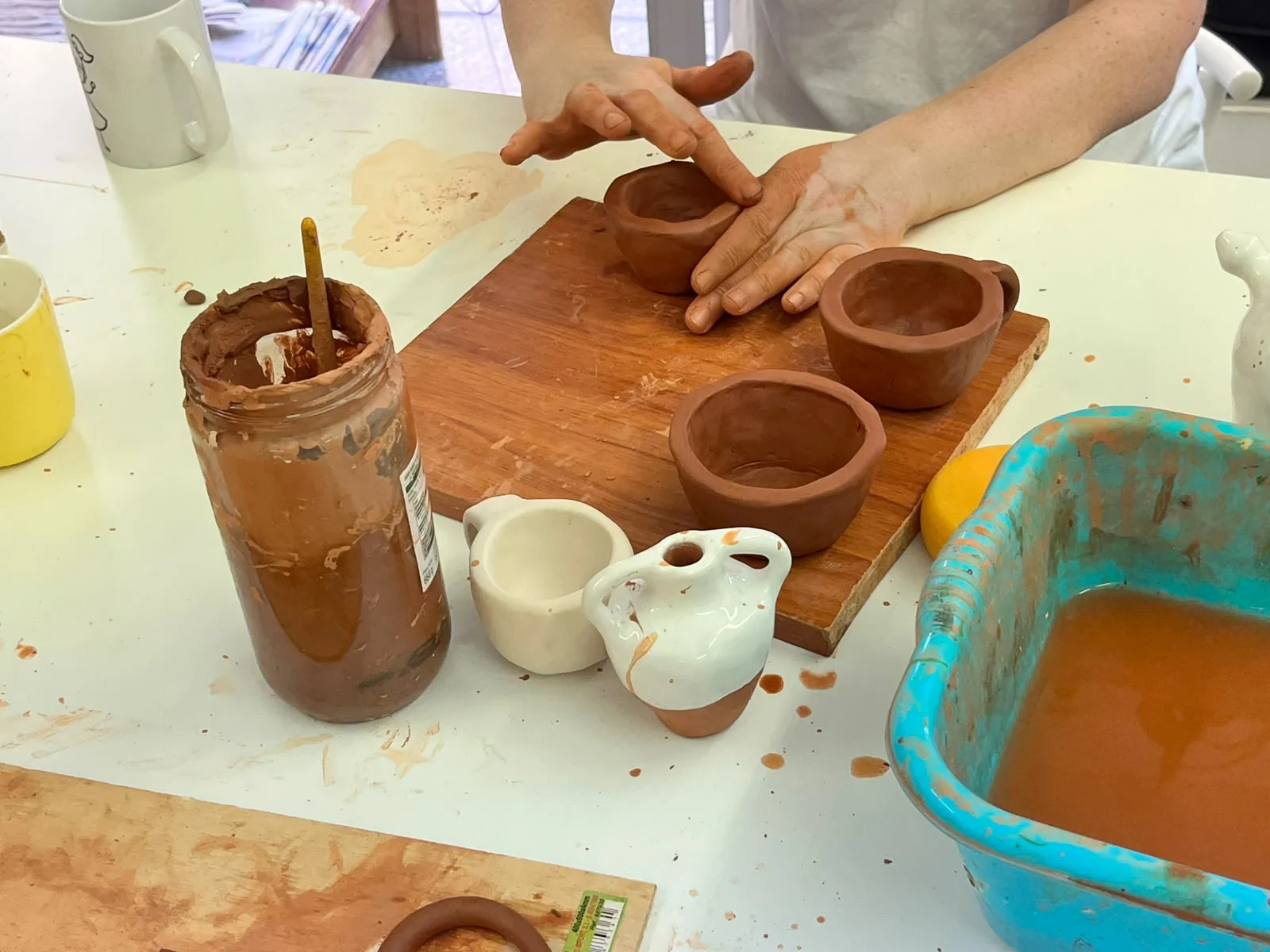 Manos modelando varios cuencos de barro sobre una tabla de madera en el taller BiGGeR